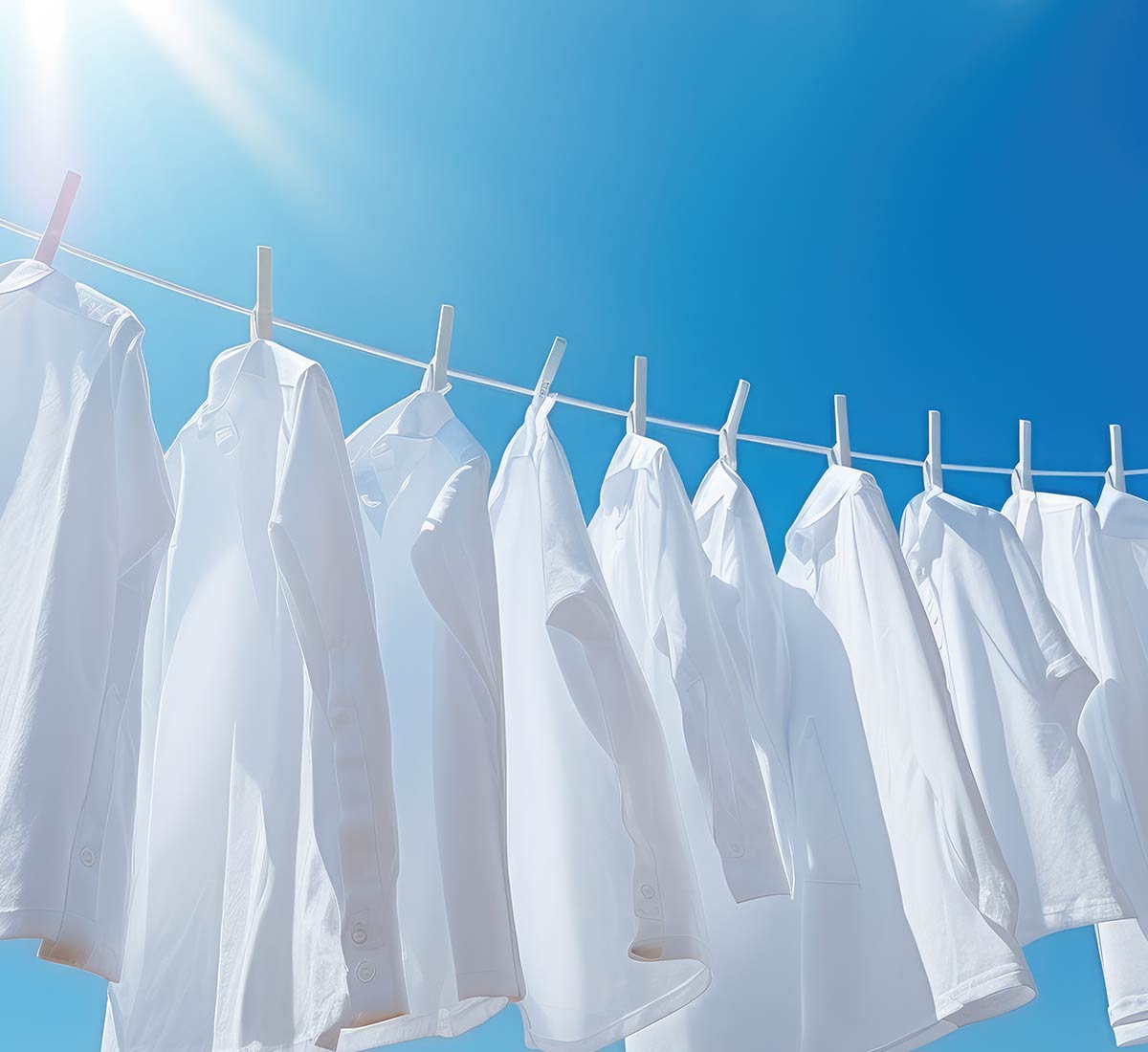 White shirts hanging on a washing line set against a blue sky with blazing sun